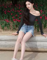 高颜值苗条美女黑色斜肩波点上衣、牛仔短裤穿着郁金香花丛旁超高清图片