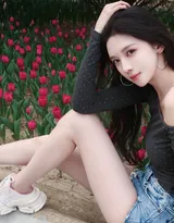 高颜值苗条美女黑色斜肩波点上衣、牛仔短裤穿着郁金香花丛旁超高清图片